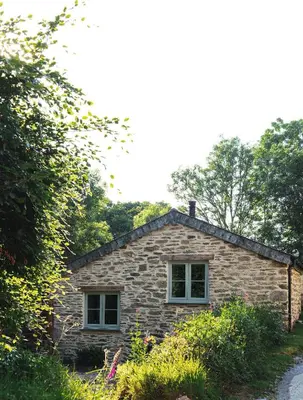 a stone house with two windows and trees at The Pigsty & Spa Garden at Tregoose Old Mill in Newquay