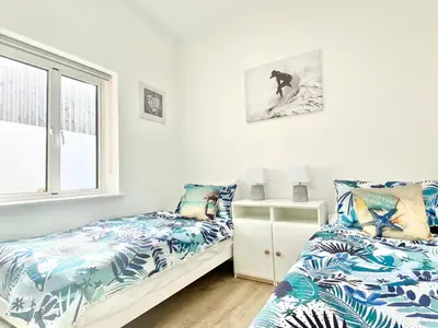 a bedroom with two beds and a window at Littlecroft, Hollywell Bay by Together Travel - Luxury Seaside Cottage Retreat in Holywell Bay