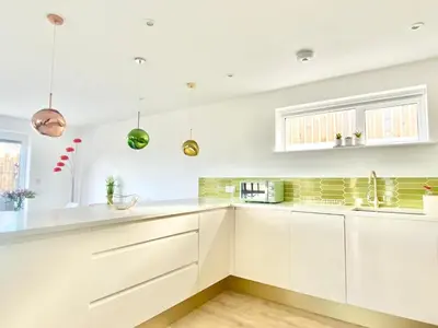 a white kitchen with white cabinets and a window at Littlecroft, Hollywell Bay by Together Travel - Luxury Seaside Cottage Retreat in Holywell Bay