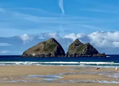a beach with two large rocks in the ocean at Littlecroft, Hollywell Bay by Together Travel - Luxury Seaside Cottage Retreat in Holywell Bay