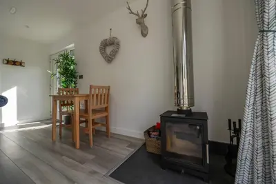 a living room with a wood stove and a table at Olverstone Lodge, a beautiful Cornish lodge with wood burner & garden in St Austell