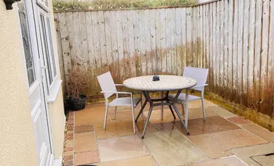 a table and chairs on a patio with a fence at Twin Gates Annexe in Falmouth