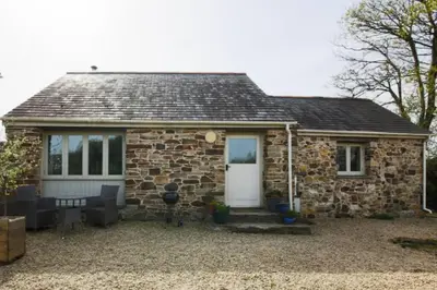 a small stone house with a white door and windows at Kiddlywink Cottage in Saint Columb Major