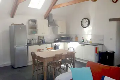 a kitchen with a table and chairs and a clock on the wall at Kiddlywink Cottage in Saint Columb Major