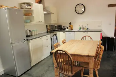 a kitchen with a table and a clock on the wall at Kiddlywink Cottage in Saint Columb Major