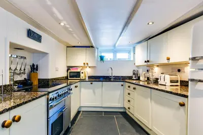 a kitchen with white cabinets and granite counter tops at Luxury Fisherman’s Cottage Historic Port Isaac in Port Isaac