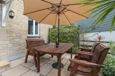 a wooden table and two chairs with an umbrella at Foxglove Cottage in Falmouth