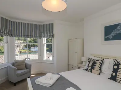 a bedroom with a bed and a chair and windows at 21 Passage Street formerly Panacea in Fowey