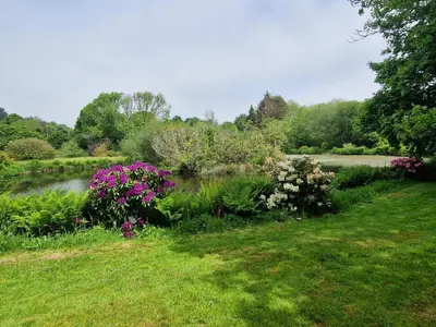 a garden with a river and flowers in the grass at Polgwedhen Lodge in Truro