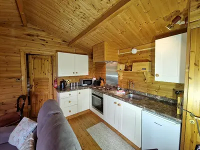 a kitchen with white cabinets and wooden walls at Polgwedhen Lodge in Truro
