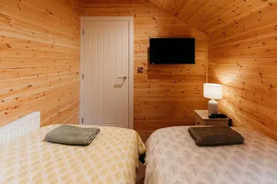 a bedroom with two beds and a tv on the wall at Riverside Retreats - Steamers Meadow in Gwinear