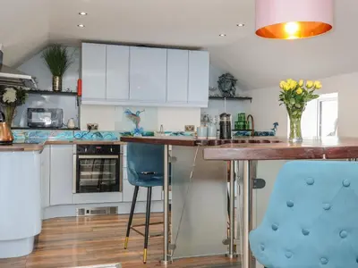 a kitchen with white cabinets and blue bar stools at Moon's Cottage in Fowey