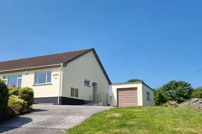 a white house with a garage on a driveway at Cornish Village Getaway in Gwennap