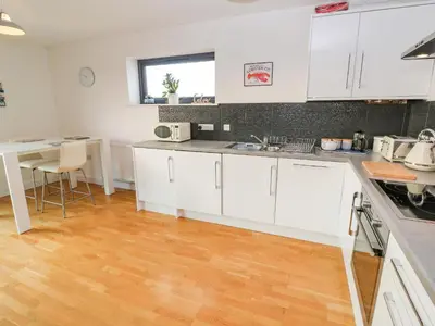 a kitchen with white cabinets and a wooden floor at Newquay, Beach Charm and Town Vibes with Parking in Newquay