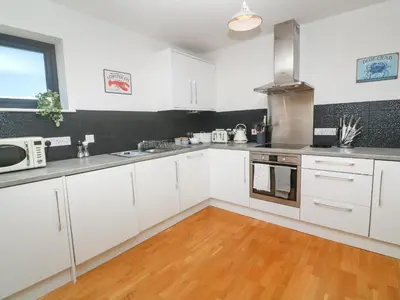 a kitchen with white cabinets and a wooden floor at Newquay, Beach Charm and Town Vibes with Parking in Newquay