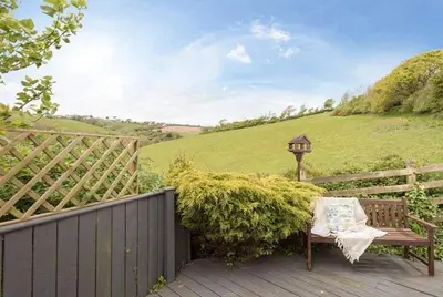 a bench on a deck with a fence and a field at Cosy Beachfront Retreat with Stunning Sea Views & Free Access to a Local Indoor Pool in Talland