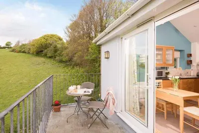 a balcony of a house with a table and a kitchen at Cosy Beachfront Retreat with Stunning Sea Views & Free Access to a Local Indoor Pool in Talland