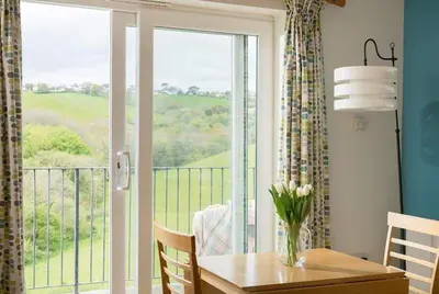 a dining room with a table and a view of a balcony at Cosy Beachfront Retreat with Stunning Sea Views & Free Access to a Local Indoor Pool in Talland