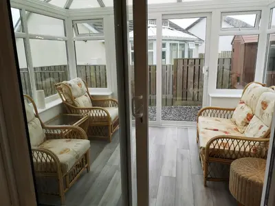 a screened in porch with wicker chairs and windows at Cornish Coastal Bungalow in Padstow