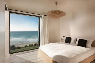 a bedroom with a large window with a view of the ocean at Little Cottage and Love Shack in Praa Sands