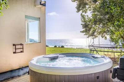 a hot tub on a patio with a view of the ocean at Little Cottage and Love Shack in Praa Sands