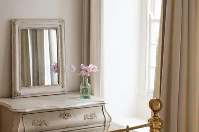 a mirror and a vase with flowers on a dresser at The Manor House in Port Isaac
