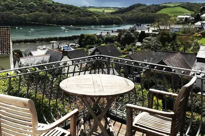 a table and chairs on a balcony with a view of a river at Stunning River Views, Tranquil Split-Level House, Private Garden & Parking in Golant