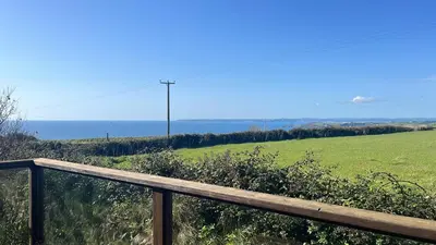 a wooden fence with a green field and the ocean at Beautiful Cornish Home 