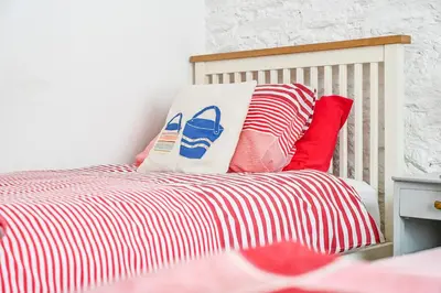 a bed with red and white striped sheets and pillows at Captain's House Looe in Looe