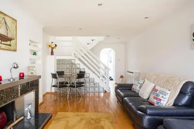 a living room with a black leather couch and a staircase at Hibiscus house in Newquay