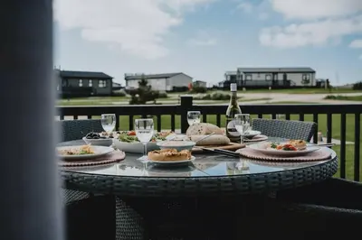 a table with plates of food and wine glasses at Cornwall Holiday Cabin with Hot tub & Sea view in Cubert