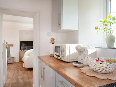a kitchen counter with a microwave and a bowl of fruit at Harlequin Cottage in St Austell