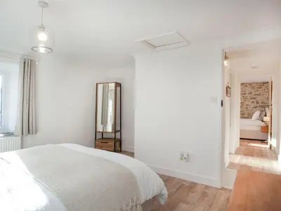 a white bedroom with a bed and a mirror at Harlequin Cottage in St Austell