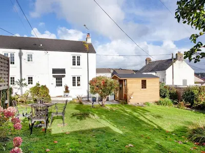 a garden with a table and chairs in front of a house at Harlequin Cottage in St Austell