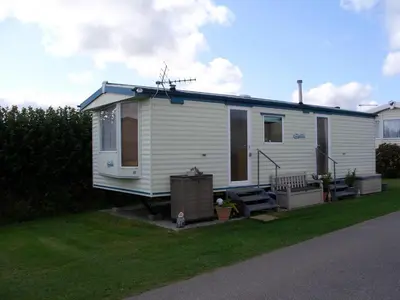 a small white house with a porch on a lawn at Colin and annioes caeravan in Looe