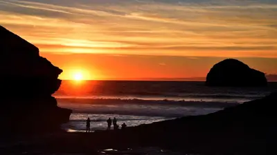 a group of people standing on a beach at sunset at Lilac Cottage Tintagel in Tintagel
