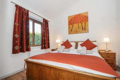 a bedroom with a bed with red curtains and a window at Lambley View in Bude
