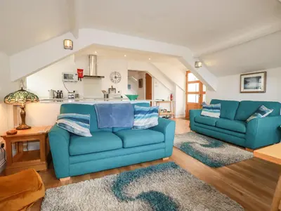 a living room with two blue couches and a kitchen at Harbour Light in Boscastle