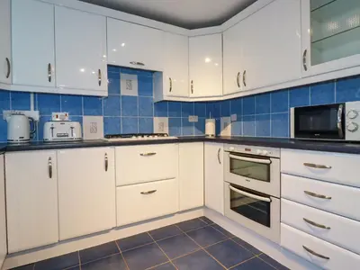 a kitchen with white cabinets and blue tiles at Seacroft in Newquay