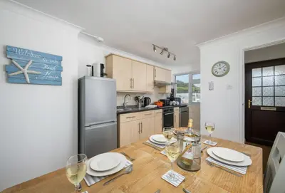a kitchen with a wooden table with plates and wine glasses at 3 Europa Court in Mawgan Porth in Mawgan Porth