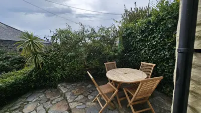 a wooden table and two chairs next to a hedge at Corner Cottage in Saint Mawes