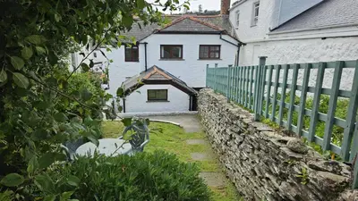 a white house with a fence and a stone wall at Hillside Cottage in Porthscatho