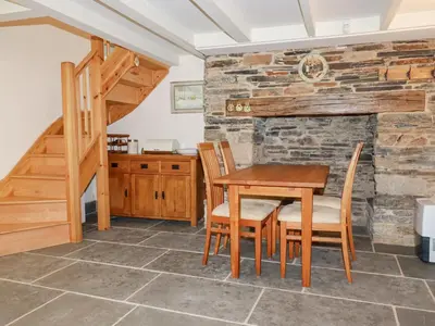 a dining room with a table and chairs and a stone wall at Mill Cottage in Liskeard
