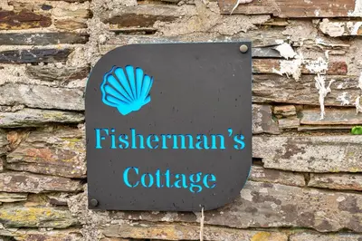 a sign on a brick wall with a sign for a felsenwegianuese college at Finest Retreats - Fishermans Cottage in Tintagel