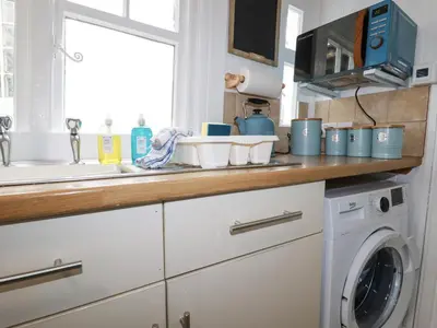 a kitchen counter with a washing machine and a window at Waves End in St Austell