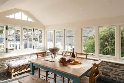 a dining room with a table and a bunch of windows at White House Cottage, Port Isaac Bay Holidays in Port Isaac
