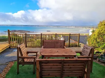 a wooden table and chairs on a balcony with a view of the ocean at 1Rosemount -Marazion - Iconic view of St Michaels Mt, Sea, Beach, 2xParking, Netflix Prime in Marazion