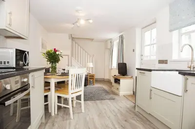 a kitchen with white cabinets and a table with chairs at Stunning cosy cottage in old town Padstow sleeps 4 in Padstow