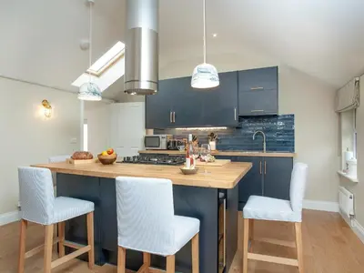 a kitchen with blue cabinets and a kitchen island with white chairs at Meadowside in Saint Mawes