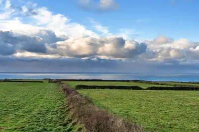 a green field with a cloudy sky and the ocean at Finest Retreats - Treknow Summerhut in Tintagel